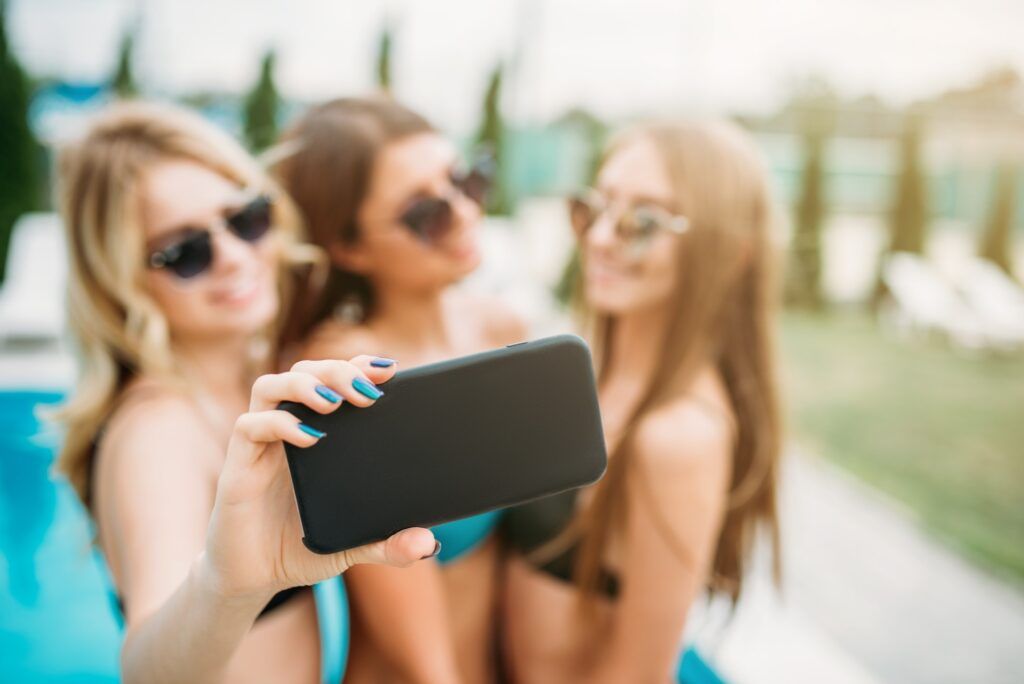 Three girls in swimsuits ad sunglasses make selfie